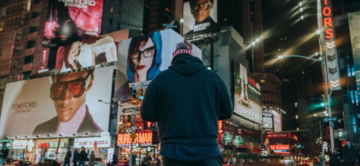 Man on street surrounded by large billboards of ads
